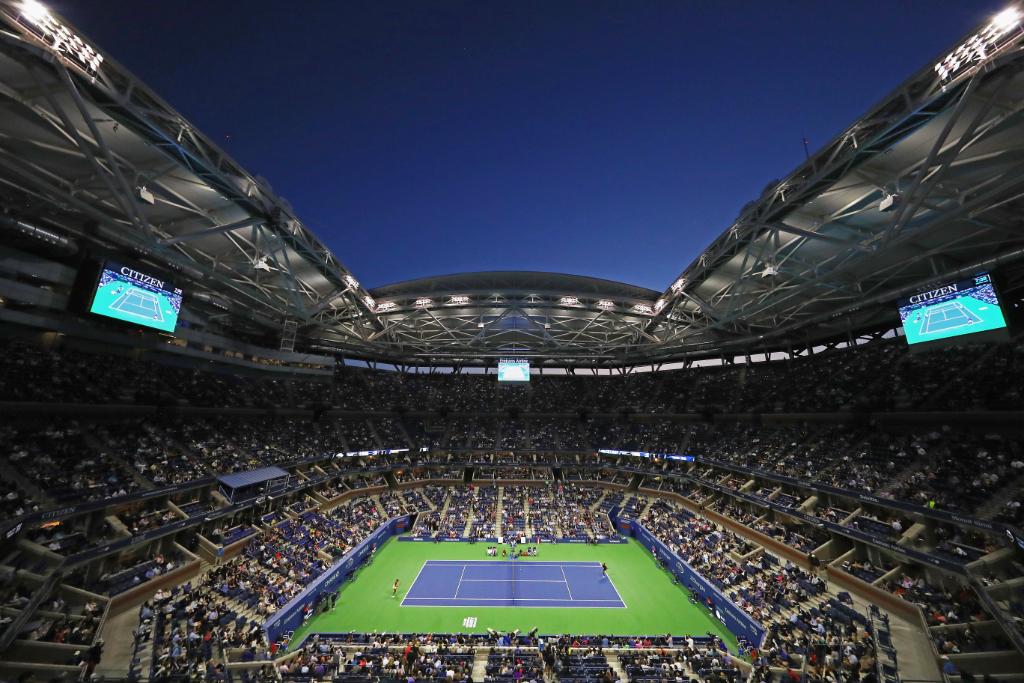 An evening match under the lights at Arthur Ashe Stadium during the US Open, with the roof open against a dark sky