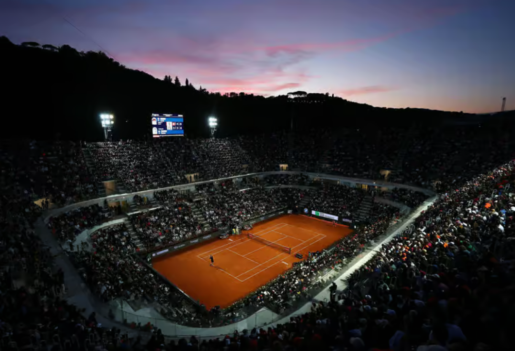 Un partido nocturno en el Campo Centrale del Abierto de Italia, bajo la luz de los focos del estadio, con el cielo oscureciéndose detrás de las gradas