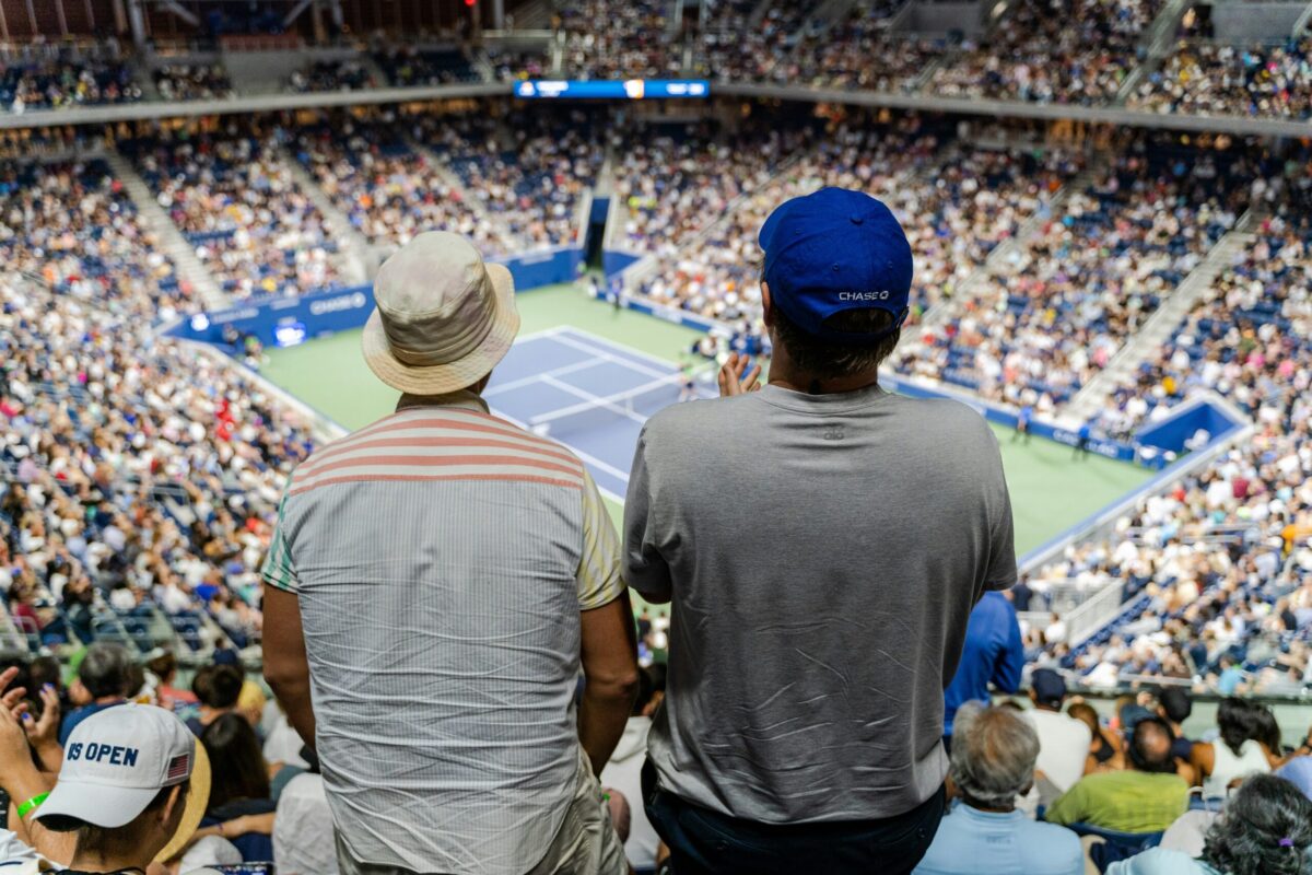 Spectators watching a match from the upper tier of Arthur Ashe Stadium at the US Open, with the blue hard court visible below
