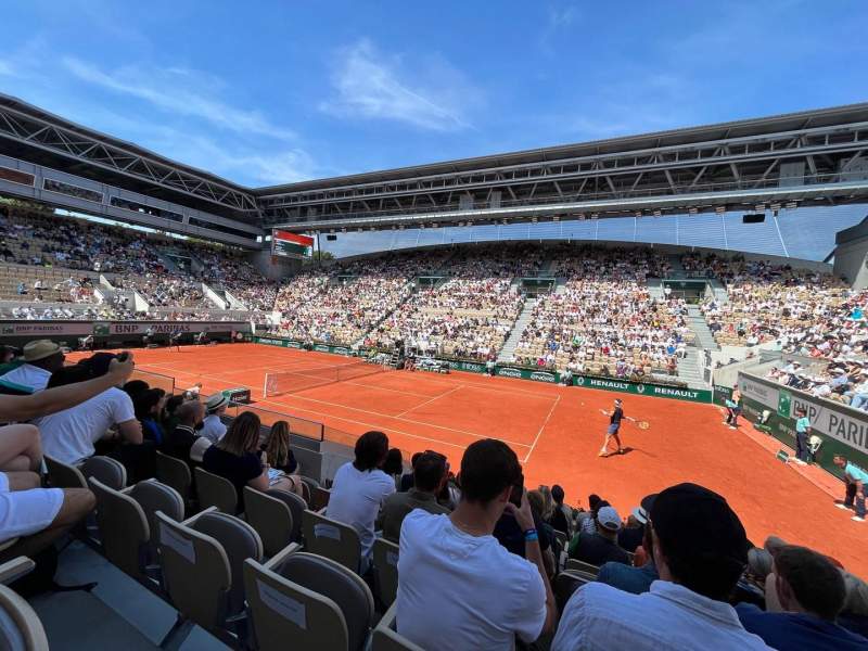 Spectators watching a match on Court Suzanne-Lenglen at Roland Garros, with the retractable roof structure visible above the stands